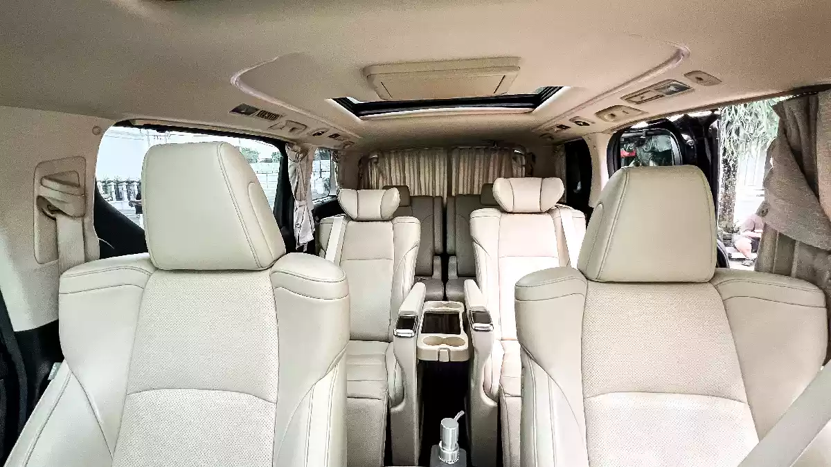 Toyota Alphard rear cabin: cream captain's chairs in row two, side curtains drawn, sunroof open