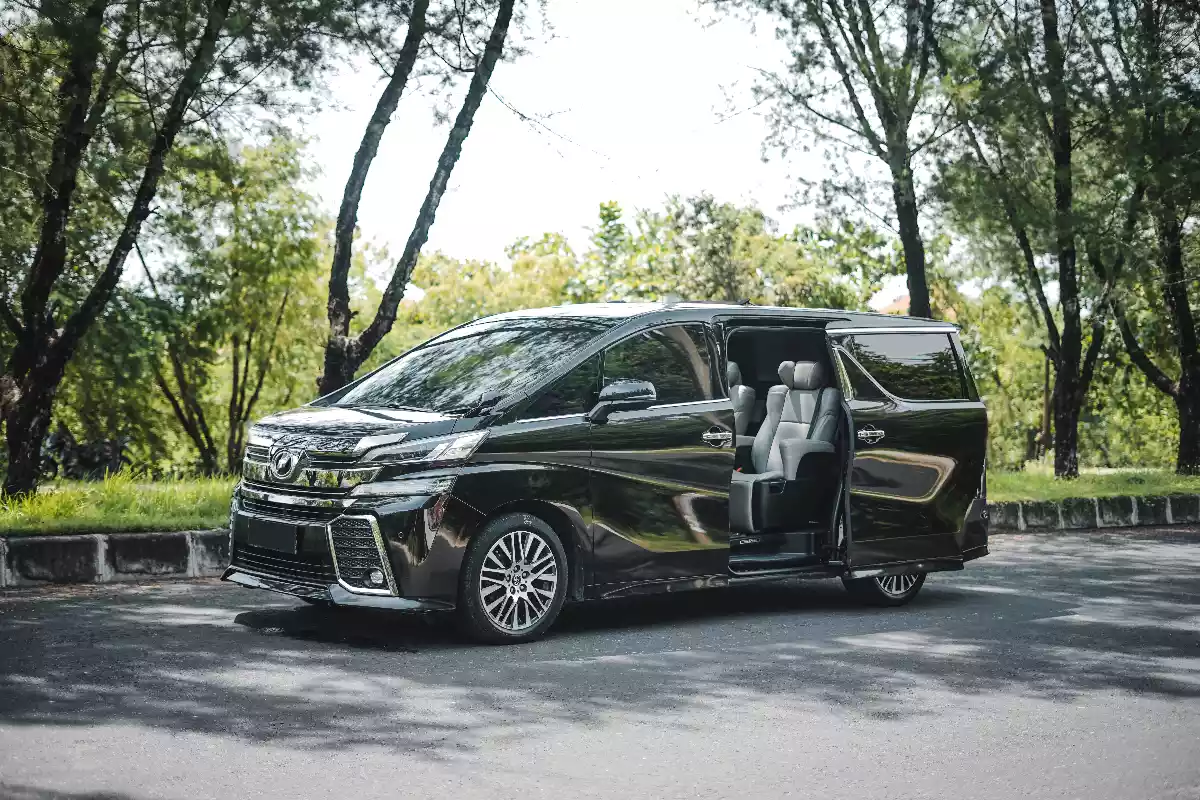 Black Toyota Vellfire on a tree-lined road with the passenger sliding door open